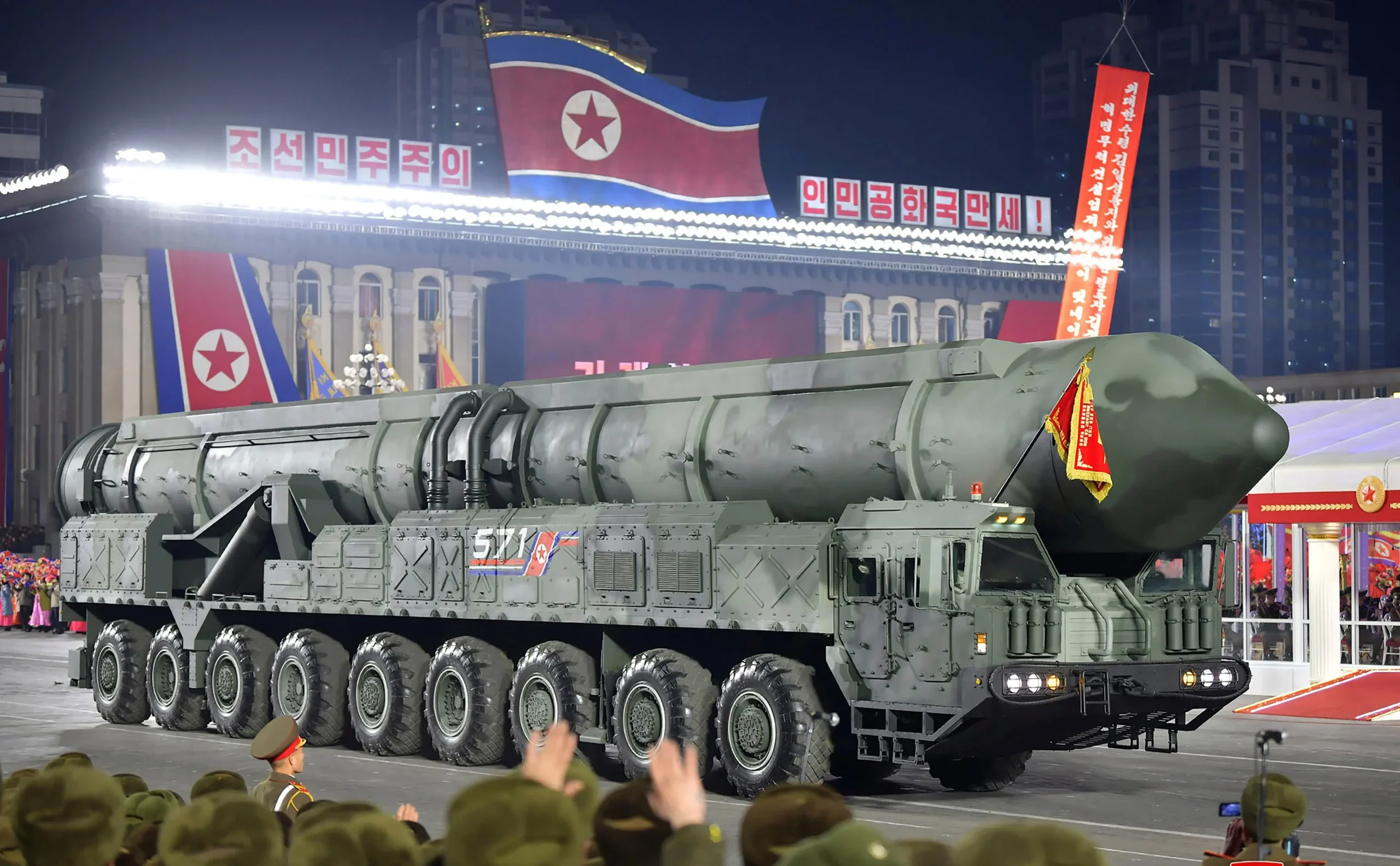North Korean military parade showcasing the Hwasong-20 ICBM on a massive launcher truck, with soldiers in formation under floodlights.