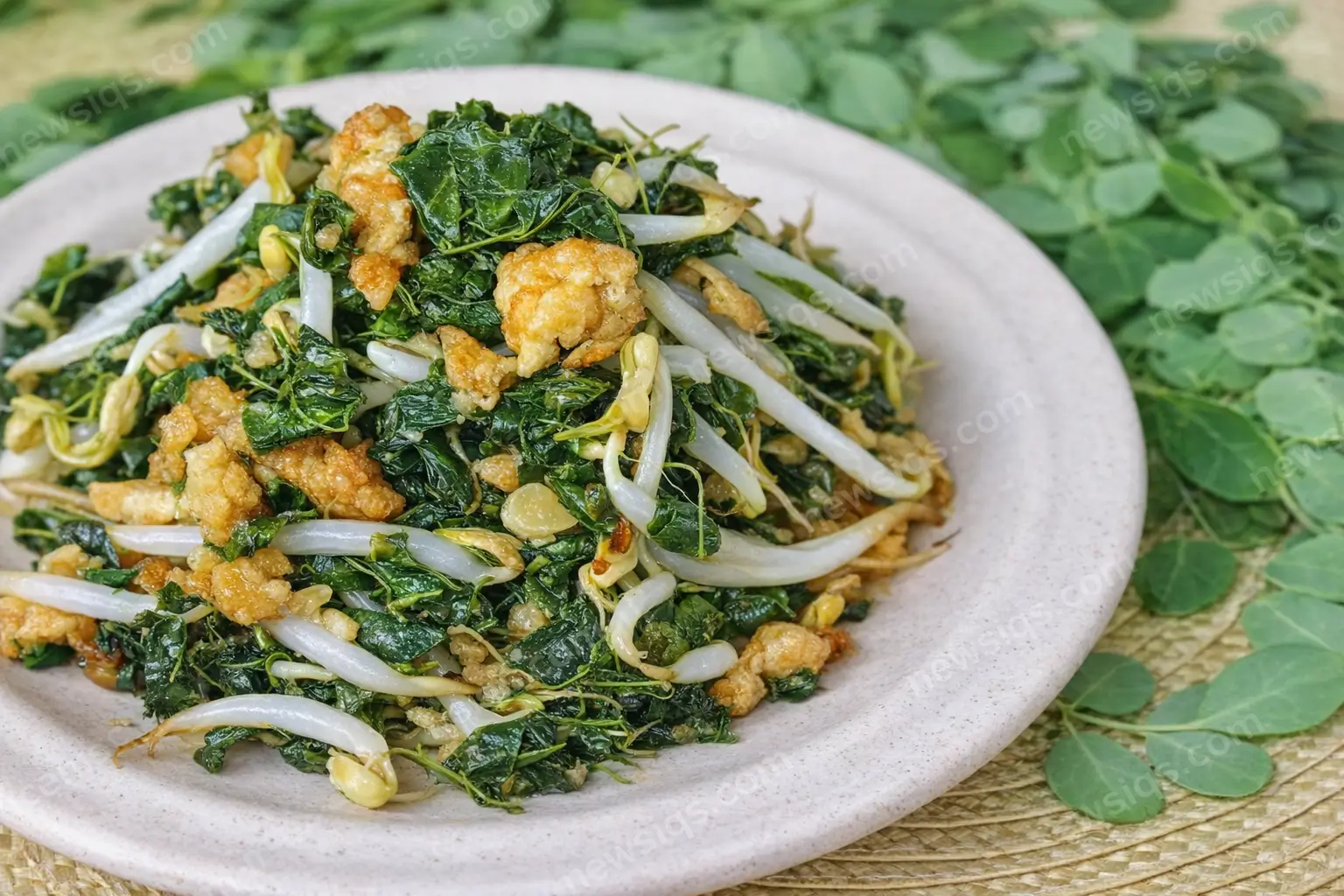 South Indian moringa leaves thoran with coconut, crunchy fried bits, and bean sprouts served on a plate with fresh moringa leaves in the background