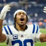 Jonathan Taylor in Indianapolis Colts white jersey number 28 celebrating with both arms raised after agreeing to new contract extension