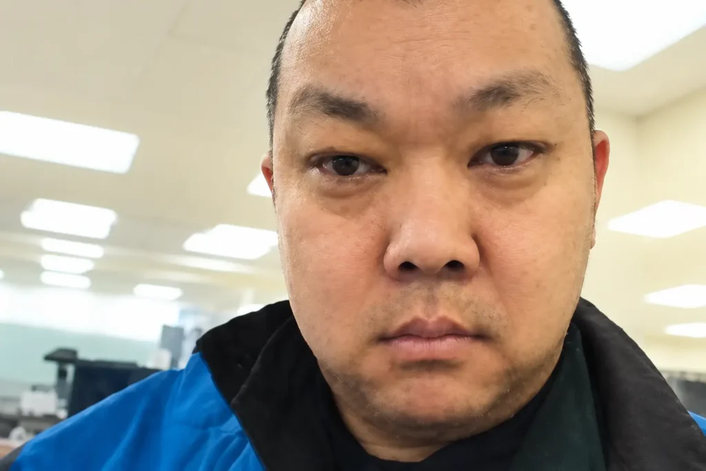 Close-up photo of Su Bin wearing a blue and black jacket indoors