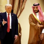 U.S. President Donald Trump in a dark suit and red tie walking alongside Saudi Crown Prince Mohammed bin Salman, who wears traditional Saudi attire, during a meeting in a formal hall.