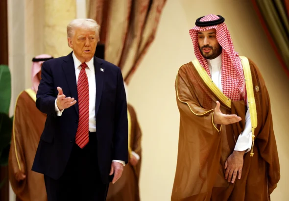 Trump Urges Muslim Leaders to Join Abraham Accords U.S. President Donald Trump in a dark suit and red tie walking alongside Saudi Crown Prince Mohammed bin Salman, who wears traditional Saudi attire, during a meeting in a formal hall.