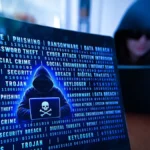 Hooded hacker using a laptop with a skull and crossbones icon, surrounded by malware and cyberattack terms - illustrating how famous hackers got caught