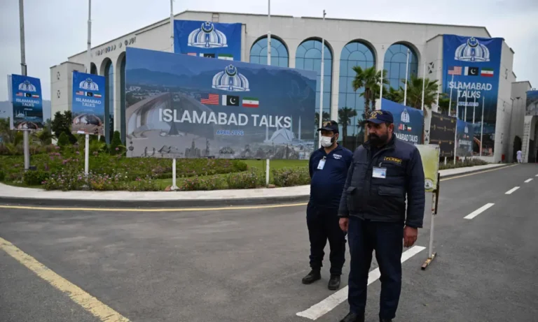 A large blue digital billboard in Islamabad displays the words "ISLAMABAD TALKS" and "APRIL 2026" against a blurred city background at dusk.