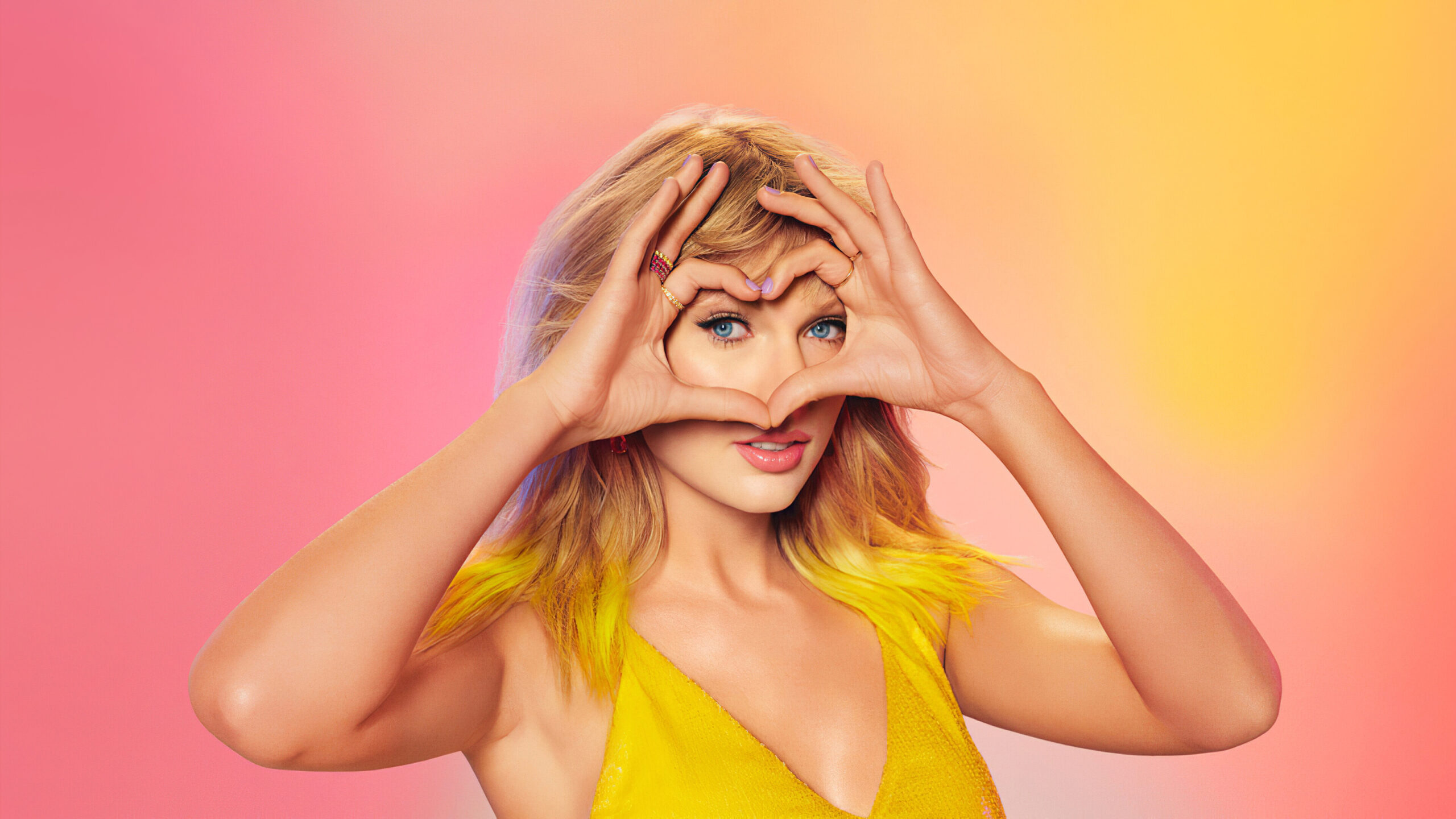 Taylor Swift making a hand heart gesture on a pink background.